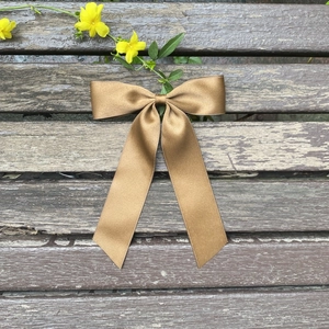 Elegant large golden brown satin bow hair clip with long ribbons on a vintage wooden bench