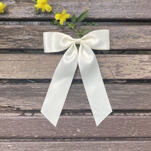 Detailed close-up of cream satin bow hair clip on a rustic wooden bench background