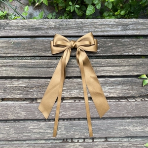 Elegant bronze satin bow hair clip with long ribbons displayed on a wooden bench