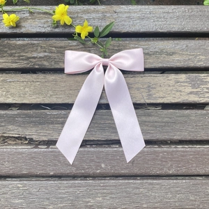 Detail of elegant pink satin ribbon bow hair clip with long tails on wood surface