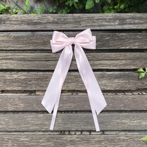Detailed view of pink satin bow with long ribbons on a rustic wood background