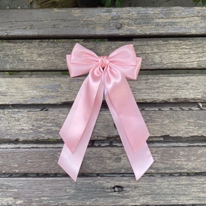 Détail d'un nœud papillon en satin rose clair avec de longs rubans sur fond bois