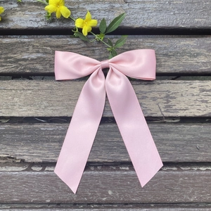 Detail of pink satin bow hair clip with long streamers on rustic wooden surface