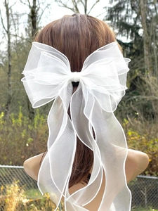 Detail of multi-layer white organza ribbon bow hairclip on model in natural lighting