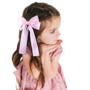 Pink satin bow hair clip with long ribbons on a young girl with brown curly hair