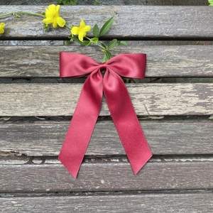 Macro shot of dark red satin bow hair clip on a rustic wooden bench with yellow flowers