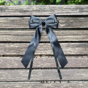 Detail of silk satin hair bow clip with long streamers on vintage wood surface