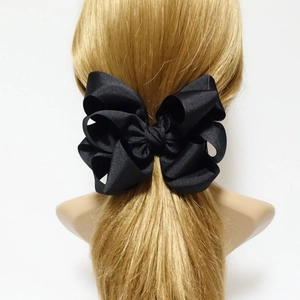 Detail of a large layered black grosgrain ribbon bow hair clip on a golden ponytail