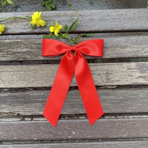 Detail of red oversized satin bow hair clip with long ribbons on rustic wood background