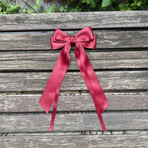 Detail of burgundy large ribbon hair clip with elegant long streamers on wood