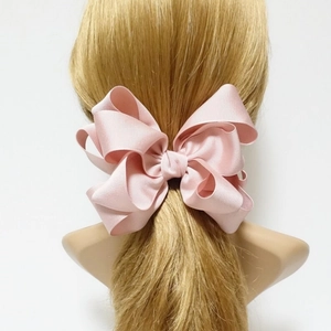 Close-up of pink layered ribbed ribbon bow clip on blonde hair showing textured fabric
