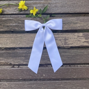 Detail of white satin ribbon bow hair clip with long streamers on wooden background