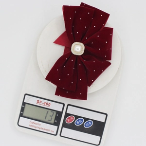 Detailed view of red velvet bow hair clip with pearl center on a digital scale