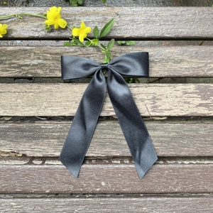 Elegant dark grey satin ribbon bow hair clip with long tails displayed on a wood bench