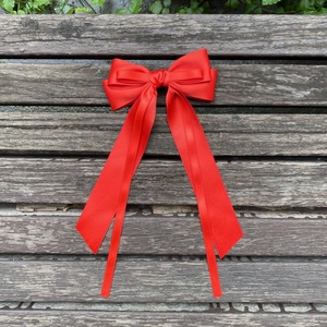 Detailed top view of large red satin bow hair clip with long ribbons on wooden surface