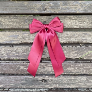 Détail d'un grand nœud papillon en satin bordeaux avec de longs rubans sur du bois