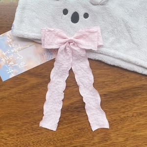 Detail of light pink pleated ribbon bow hair clip with long streamers on wooden background