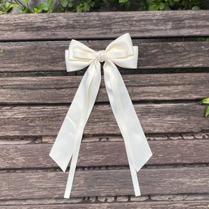 Detailed close-up of a cream white satin bow hair clip with long elegant ribbons