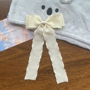 Detail of a creamy ruffled ribbon bow hair clip with long streamers on a wooden table