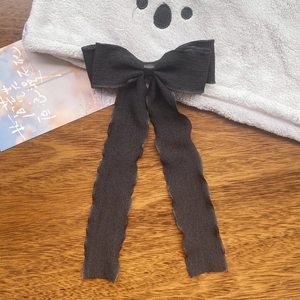 Detailed view of black pleated ribbon bow hairclip with long flowing streamers on wooden surface