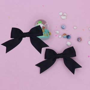 Detail of two black grosgrain ribbon bow hair clips with swallowtail design on pink surface