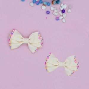 Close-up of cream ribbed ribbon hair bows with rainbow confetti edges on pink background