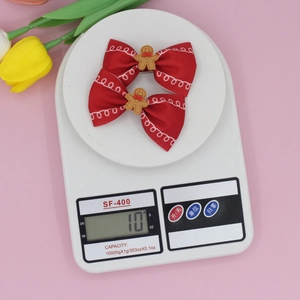 Pair of red bow hair clips with gingerbread man charms on a digital scale weighing 10g