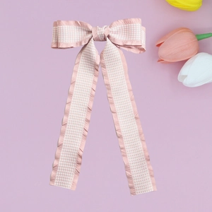 Detail of pink houndstooth bow hair clip with ruffled edges on light purple background