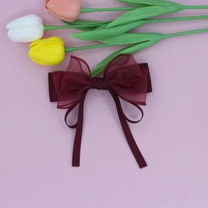 Detail of burgundy mesh layered bow hair clip with long ribbons on pink background
