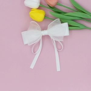 Elegant white mesh bow hair clip with long ribbons on soft pink background