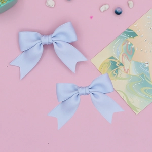 Close-up of light blue ribbon bow hair clips set on a decorative soft pink background