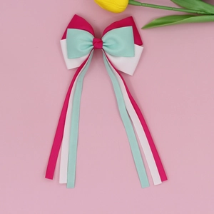 Macro detail of tricolor ribbed bow hair clip with streamers on a pink background