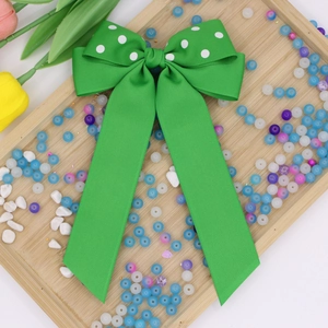 Dettaglio di un grande fiocco per capelli in gros-grain verde a pois bianchi con nastri