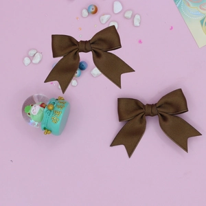 Detail view of two dark brown ribbon bow hair clips with swallowtail design on pink surface