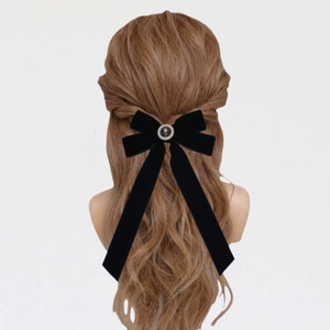 Detail of black velvet bow hair clip with vintage pearl center on wavy brown hair
