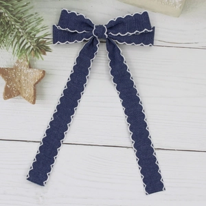 Gros plan du nœud en denim bleu foncé avec broderie ondulée blanche sur fond en bois