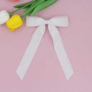 Detail of white lace hair clip bow featuring long flowing ribbons and delicate floral patterns