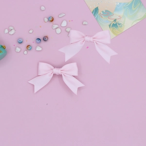 Pair of sweet pink grosgrain ribbon swallowtail bow hair clips for girls set on pink background