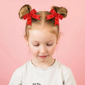 Pair of red satin bow hair clips for kids on a girl with symmetrical buns and pink background