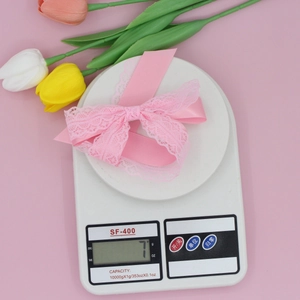 Pink lace ribbon bow hair clip weighing 7g on a white scale with tulip decor