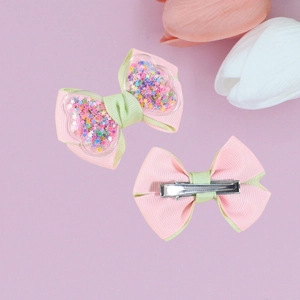 Pink and green quicksand bow hair clips with glitter stars on a purple floral background