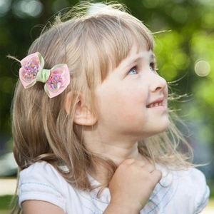 Sweet pink and green bow hair clip with colorful sequins worn by a girl outdoors