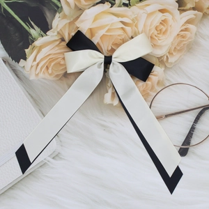 Close-up of dual-layer black and white satin bow hair clip on a soft plush surface