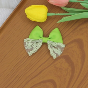 Detailed close-up of a double-layered green lace bow hair clip on a wooden texture background