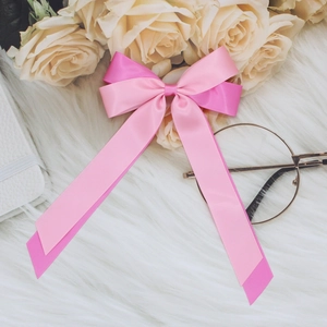 Close-up of dual-tone pink satin ribbon bow with glossy finish on soft white plush fabric
