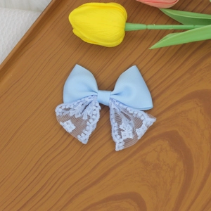 Detail of light blue bow hair clip featuring delicate white floral embroidery and lace