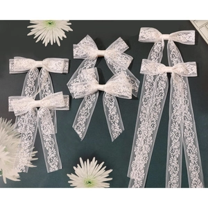 Detail of white embroidery lace bow hair clips with long ribbons on dark green background