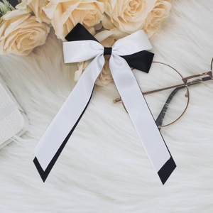 Detail of black and white satin ribbon bow hair clip with streamers on a soft plush background