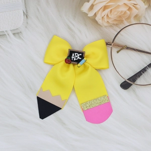 Detail showing school-themed yellow pencil bow hair clip with ABC blackboard and red apple