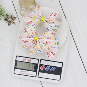 Two-piece children white bow hair clips with colorful letter prints on white wood surface